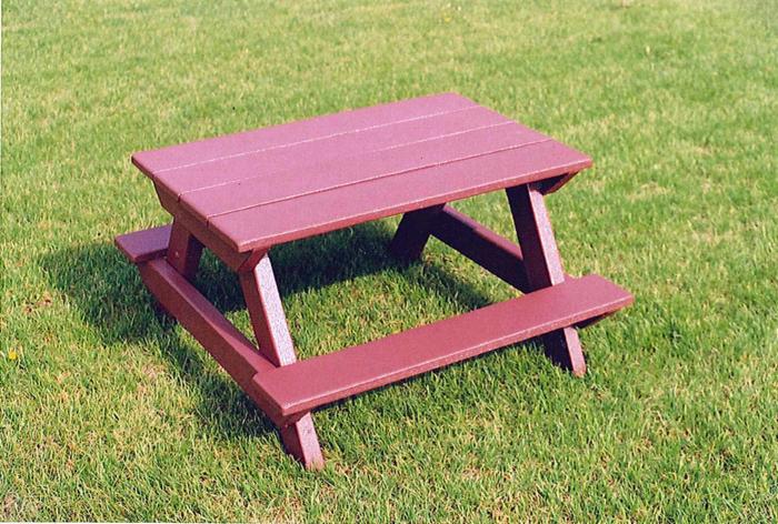 Mały, pomalowany na bordowo stolik piknikowy dla dzieci z tworzywa sztucznego, ustawiony na trawie w słoneczny dzień.