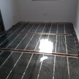 Montaż mat grzewczych Termofol we Włocławku, widoczne ułożone pasy na podłodze w pustym pomieszczeniu, przygotowane do dalszych prac wykończeniowych.