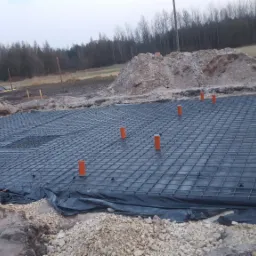 Przygotowanie zbrojenia pod wylewkę na folii budowlanej, widoczne wystające rury instalacyjne.