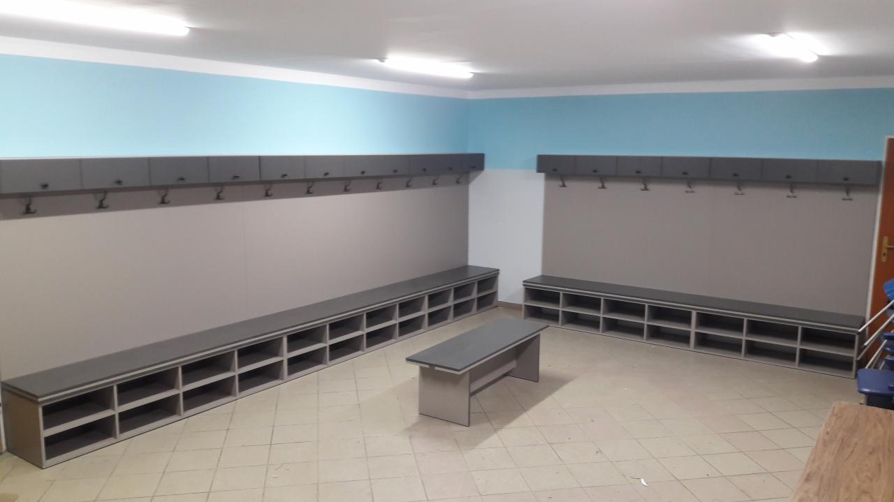 Szara szatnia z ławkami i szafkami z wieszakami, jasna podłoga z płytek, niebieski pas na ścianie