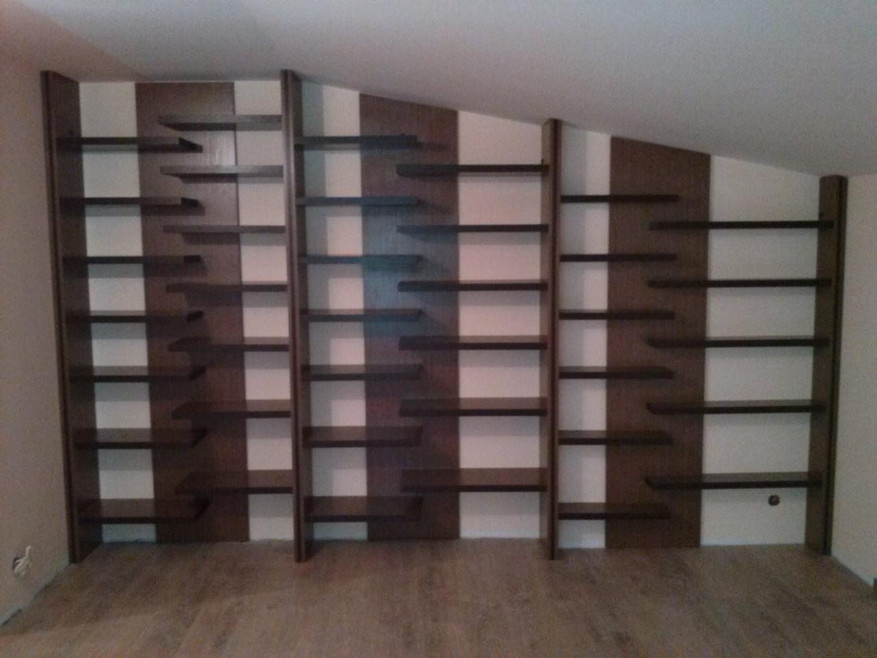 Zabudowa wnęki z ciemnobrązowymi półkami na książki, dopasowana do skosu sufitu, widok z dołu.