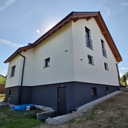 Usługi Remontowo Budowlane '' WalBud '' Walura Łukasz - Dwukolorowa elewacja domu jednorodzinnego w słoneczny dzień. Jasna góra i ciemny dół, widoczne okna i elementy drewniane dachu. Ujęcie z dołu, podkreślające bryłę budynku.