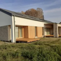 Nowoczesny dom jednorodzinny z elementami drewnianymi i kamienną elewacją, widok z zewnątrz w słoneczny dzień.