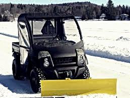 Czarny pojazd Kawasaki MULE 4010 DIESEL 4X4 z żółtym pługiem do śniegu na ośnieżonej drodze w zimowym krajobrazie.