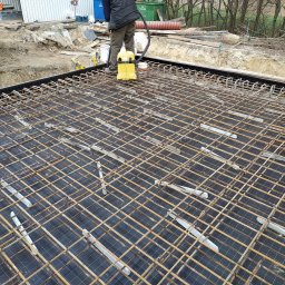 EXPRESS- BUD SPÓŁKA Z OGRANICZONĄ ODPOWIEDZIALNOŚCIĄ - Zbrojenie fundamentów domu jednorodzinnego z widocznymi podkładkami dystansowymi i żółtym odkurzaczem przemysłowym. Prace przygotowawcze do wylania betonu.