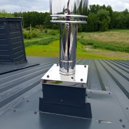 EXPRESS- BUD SPÓŁKA Z OGRANICZONĄ ODPOWIEDZIALNOŚCIĄ - Błyszczący, chromowany komin wentylacyjny na szarym dachu z blachy trapezowej. W tle zielone drzewa i pochmurne niebo. Widoczne śruby mocujące.