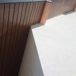 Wykończenie elewacji budynku w Olecku z drewnianą podbitką i białą, chropowatą strukturą tynku.