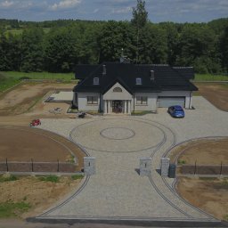 KASBUD Prace Brukarskie Kacper Jaszczerzewski - Rozległa posesja z domem jednorodzinnym i ozdobnym podjazdem z kostki brukowej. Widok z lotu ptaka ukazuje okrągły wzór i symetryczne ścieżki.