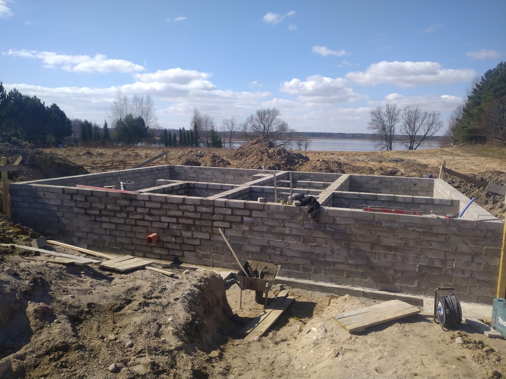 Wznoszenie ścian fundamentowych z bloczków betonowych na placu budowy z widokiem na jezioro w tle.