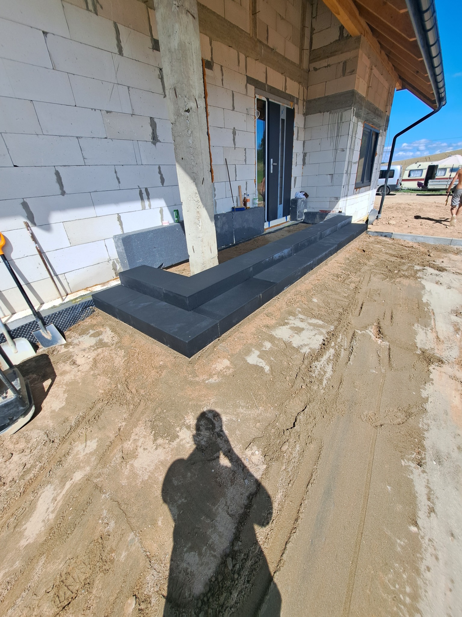 Nowe, grafitowe schody wejściowe z kostki brukowej prowadzące do domu w stanie surowym w Olecku. Widoczny cień osoby robiącej zdjęcie.