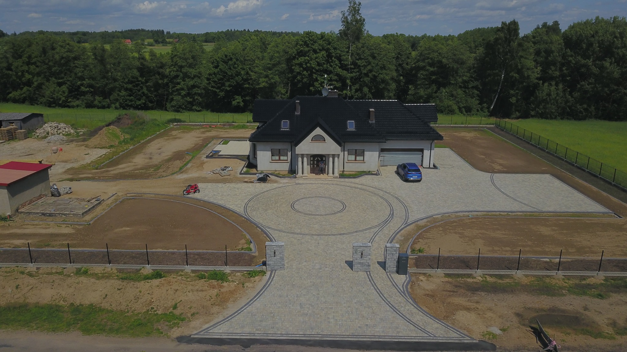 Rozległa posesja z domem jednorodzinnym i ozdobnym podjazdem z kostki brukowej. Widok z lotu ptaka ukazuje okrągły wzór i symetryczne ścieżki.
