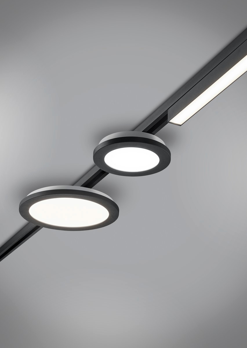 Oświetlenie szynowe z dwoma okrągłymi reflektorami LED i jednym prostokątnym, zamontowane na szarej powierzchni sufitu, ukazane z perspektywy żabiej.