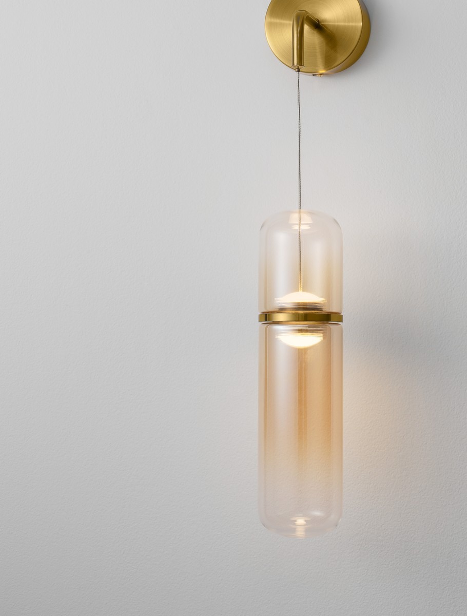 Szklany kinkiet ścienny w odcieniach bursztynu i złota, z delikatnym światłem, zawieszony na tle jasnej ściany. Minimalistyczny design, eleganckie wykończenie.