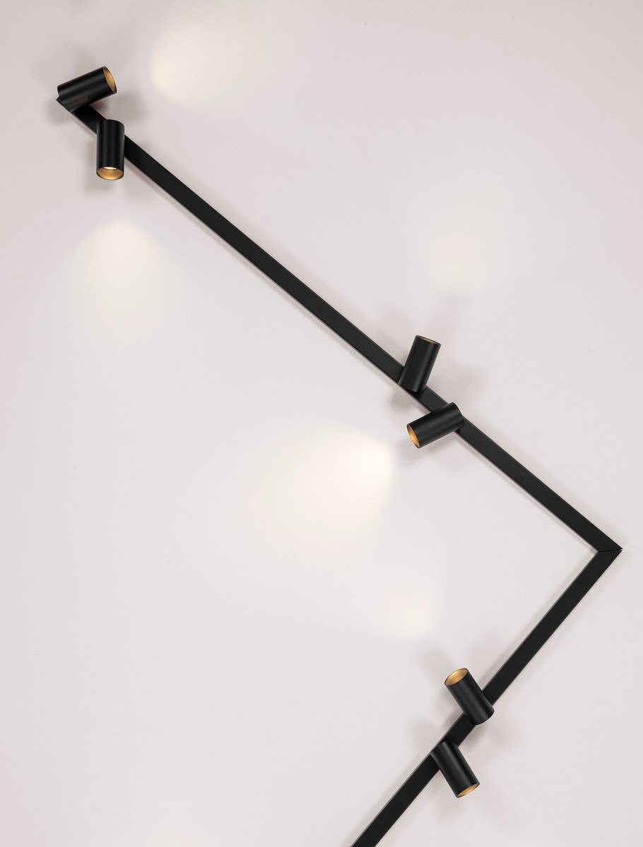 Czarna, nowoczesna lampa sufitowa z reflektorami punktowymi, zamontowana na białym suficie, oświetlająca przestrzeń ciepłym światłem.