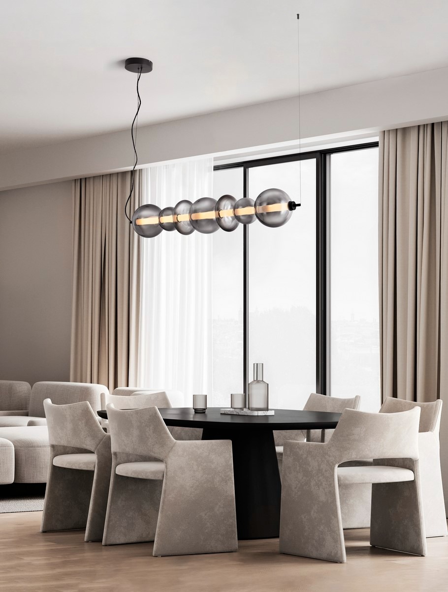 Nowoczesna lampa wisząca z szarymi, szklanymi kulami nad okrągłym stołem jadalnym w minimalistycznym wnętrzu. Stonowana kolorystyka, duże okno.