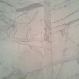 Ściana wyłożona białym marmurem z szarymi żyłami, widoczny narożnik.