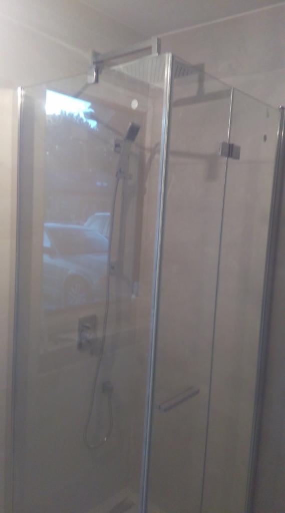 Kabina prysznicowa z deszczownicą i baterią, widoczne odbicie samochodu na szklanej powierzchni.