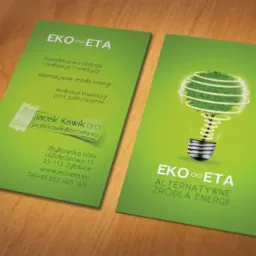 Dwie zielone wizytówki firmy EKO ETA na drewnianym tle. Jedna wizytówka zawiera dane kontaktowe i adres, a druga logo firmy: żarówka z roślinnym wnętrzem symbolizująca alternatywne źródła energii.