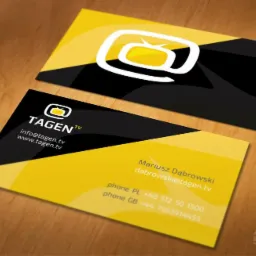 Dwie wizytówki firmy Tagent TV z nowoczesnym logo w kształcie telewizora w okręgu, utrzymane w kolorystyce żółto-czarnej, leżące na drewnianym blacie.