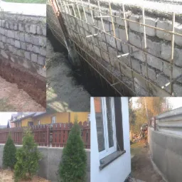 Montaż zbrojenia przy betonowym murze oporowym, widoczne etapy budowy i wykop. Fragment domu z oknem w tle.