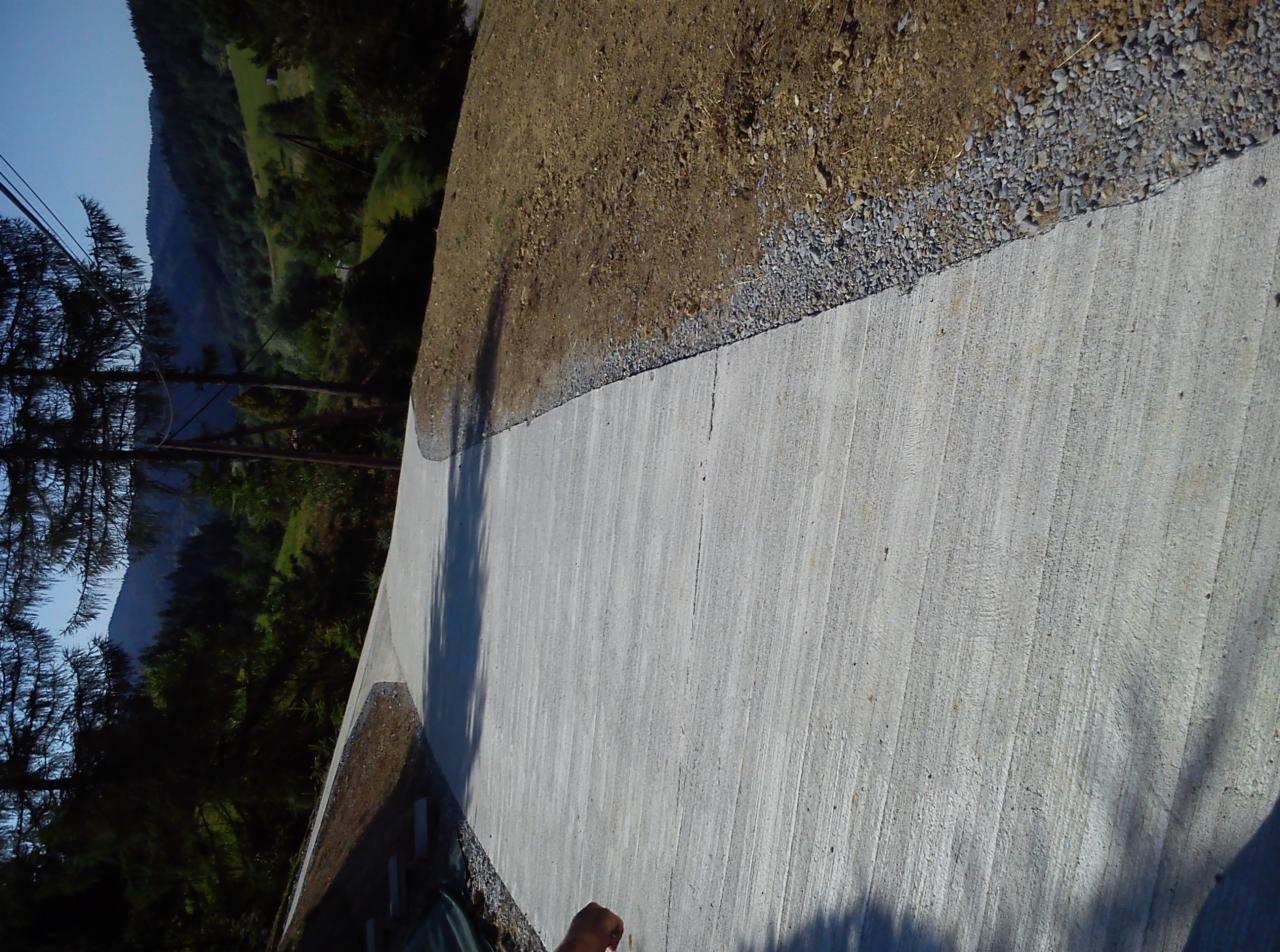 Betonowa droga przez górski teren, z widocznym obrzeżem z kamieni i zboczem. W tle zalesione wzgórza. Ujęcie z góry, obrócone o 90 stopni.