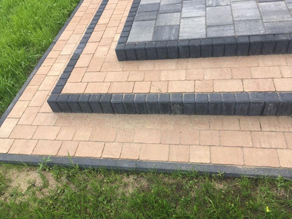 Schody z kostki brukowej w odcieniach beżu i grafitu, otoczone zieloną trawą, wykonane w Pruszczu Gdańskim. Widoczne detale ułożenia kostki i jej faktura.
