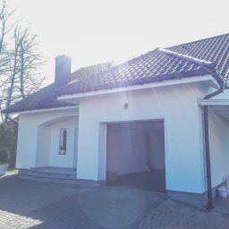 Damian Hołojda Firma Handlowo-Usługowa Profibud - Biały dom jednorodzinny z garażem i podjazdem z kostki, po renowacji elewacji. Widoczne drzewa bez liści w tle i samochody po bokach.