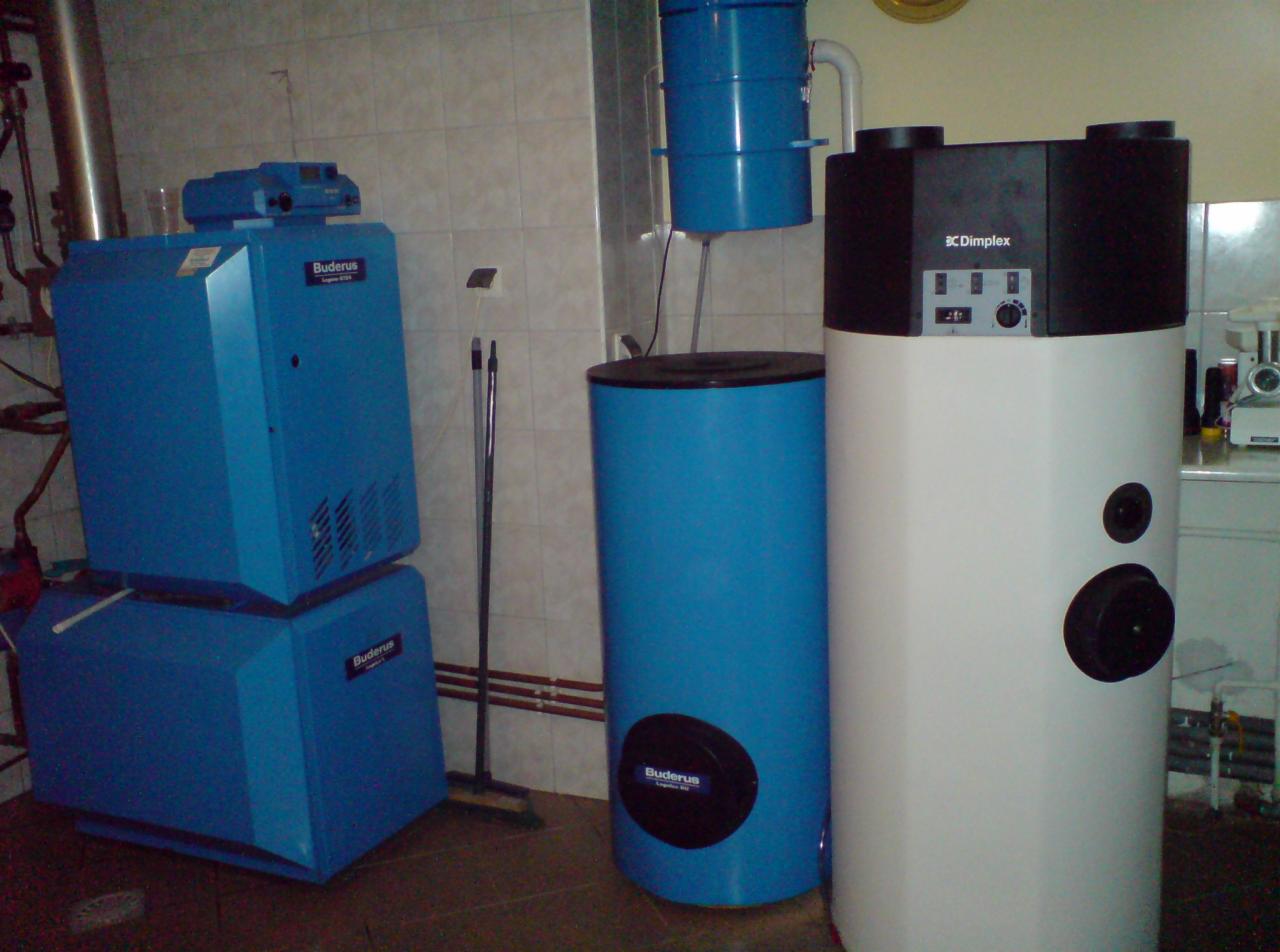 Zestaw urządzeń grzewczych: niebieski piec Buderus, zbiornik buforowy i biały zasobnik Dimplex w kotłowni z wykafelkowanymi ścianami. Widoczna instalacja rurowa.