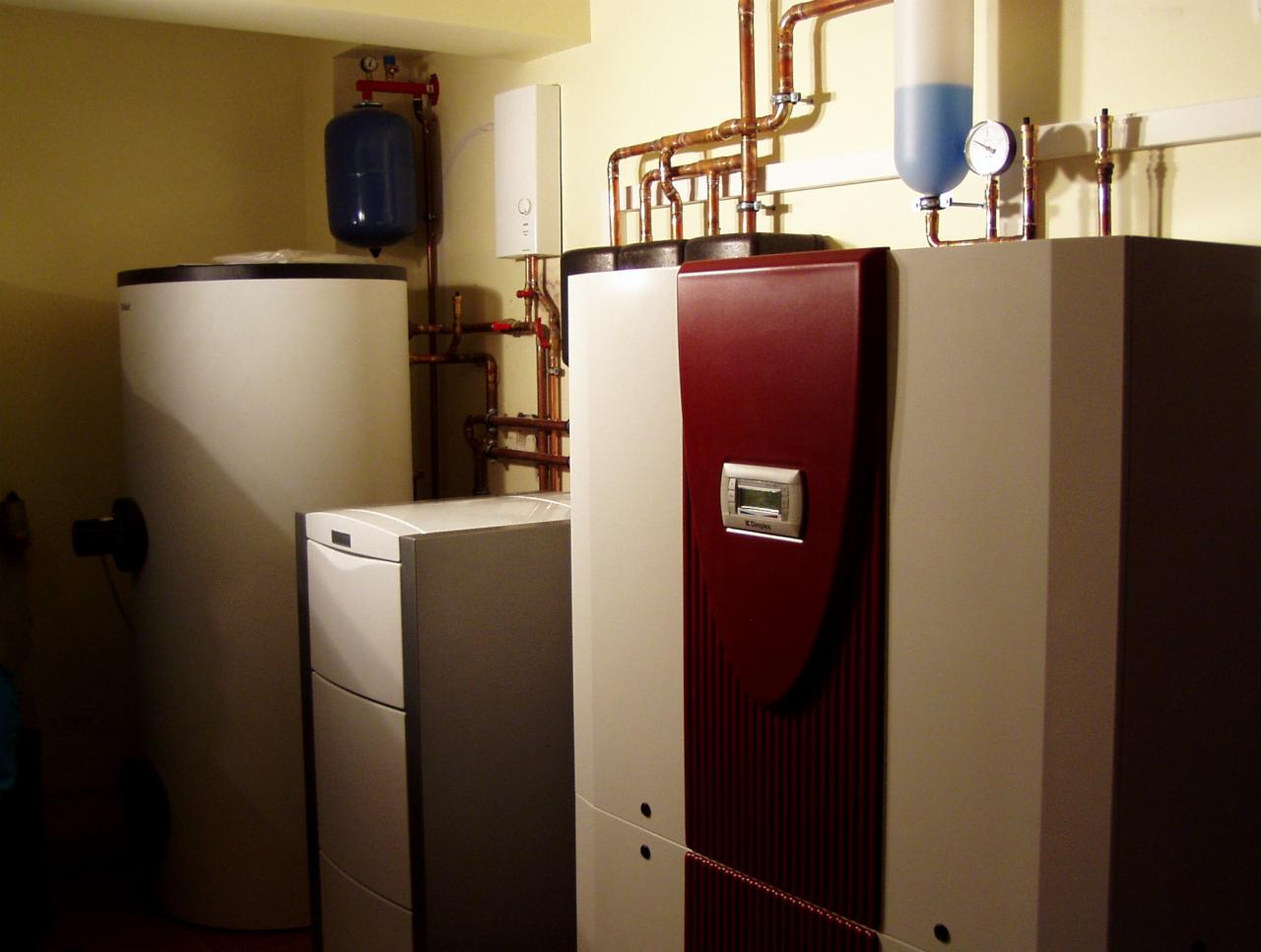 Zestaw urządzeń grzewczych w kotłowni: zbiornik buforowy, pompa ciepła z bordowym panelem, naczynie przeponowe i instalacja z miedzianych rur.