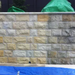 Fragment kamiennej ściany po czyszczeniu, z widocznymi różnicami w kolorze kamieni. Część ściany jaśniejsza, sugerująca świeżo zakończony proces czyszczenia.