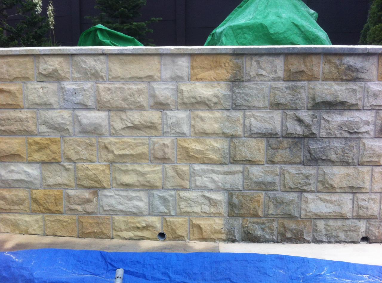 Fragment kamiennej ściany po czyszczeniu, z widocznymi różnicami w kolorze kamieni. Część ściany jaśniejsza, sugerująca świeżo zakończony proces czyszczenia.