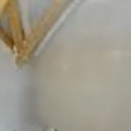 Szczegółowe ujęcie fragmentu drewnianej konstrukcji, prawdopodobnie tarasu lub balkonu, z widocznymi elementami mocującymi i jasną, betonową powierzchnią w tle.