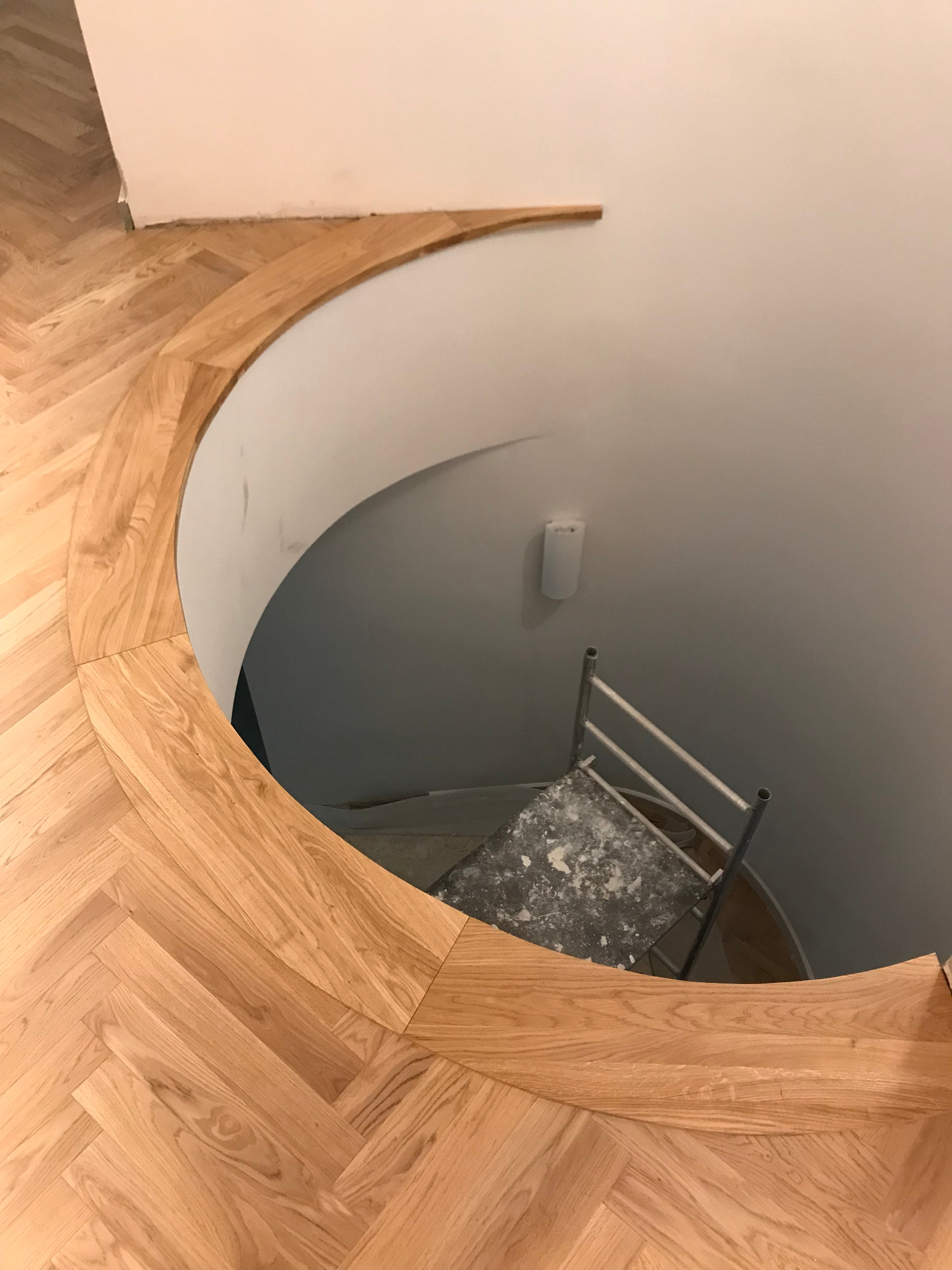 Układanie parkietu w jodełkę na schodach spiralnych, widoczny fragment ściany i drabina malarska z resztkami zaprawy.