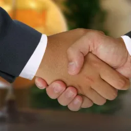 Uścisk dłoni dwóch mężczyzn na tle rozmytej mapy świata i zieleni, symbolizujący zawarcie umowy.