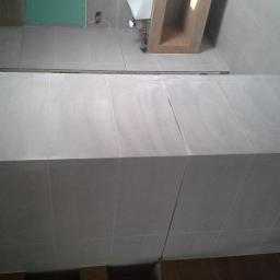 Jacek Rzepka Usługi Remontowo Budowlane - Wykończona powierzchnia z płytek w łazience w Miliczu. Jasne, kwadratowe płytki ułożone na ścianie i podłodze, widoczne fugi. Minimalistyczny design.