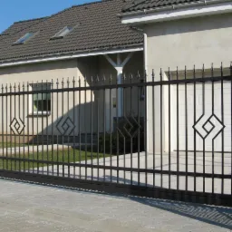 Elegancka, przesuwna brama wjazdowa z czarnymi, pionowymi prętami i dekoracyjnym motywem rombu, na tle domu z garażem i zadbanym trawnikiem.