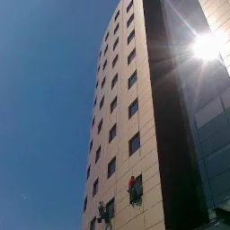 Trzech alpinistów przemysłowych myje okna na elewacji wysokiego biurowca w słoneczny dzień, widok z dołu.