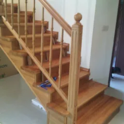 Jasne, drewniane schody z balustradą, widok z dołu, z narzędziami na jednym ze stopni. Naturalne oświetlenie podkreśla teksturę drewna.