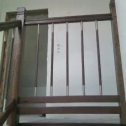 Fragment balustrady schodowej z drewna i metalu w Brzeźnicy. Ciemne drewno i pionowe, metalowe pręty tworzą elegancki detal architektoniczny.