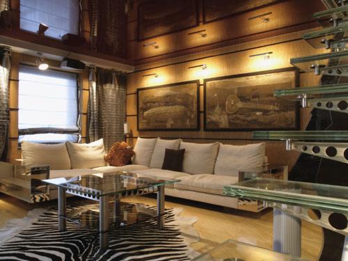 Nowoczesny salon w Łodzi z kanapą, szklanym stolikiem i schodami. Wyjątkowy dywan w zebrę dodaje charakteru. Oświetlenie punktowe podkreśla dekoracje ścienne.