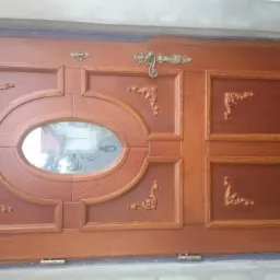 Drewniane drzwi wejściowe z owalnym przeszkleniem i dekoracyjnymi ornamentami, zamontowane w surowym otworze, widoczne ślady prac wykończeniowych.