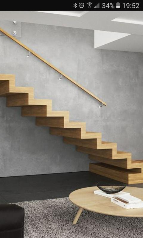 Nowoczesne, drewniane schody wspornikowe z minimalistyczną balustradą przymocowaną do szarej ściany, widoczne z perspektywy salonu z okrągłym stolikiem kawowym.