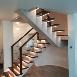 Nowoczesne schody z podświetlanymi stopniami i szklaną balustradą w domu w Rząśni, widok z dołu.