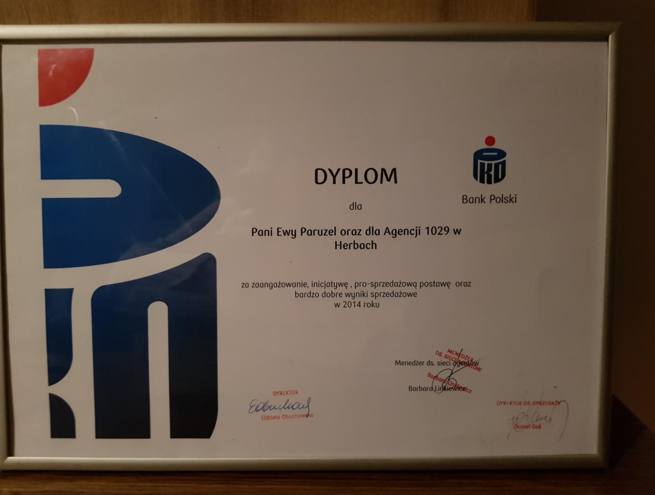 Oprawiony dyplom uznania dla Pani Ewy Paruzel i Agencji 1029 w Herbach od Banku Polskiego za zaangażowanie i dobre wyniki sprzedażowe w 2014 roku, widoczne podpisy dyrektorów i logo banku.
