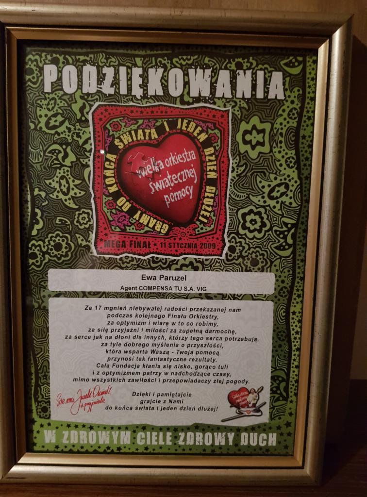 Oprawione w złotą ramę podziękowanie dla agenta ubezpieczeniowego COMPENSA TU S.A. VIG, Ewy Paruzel, od Wielkiej Orkiestry Świątecznej Pomocy za wsparcie podczas finału. Dokument zawiera tekst...