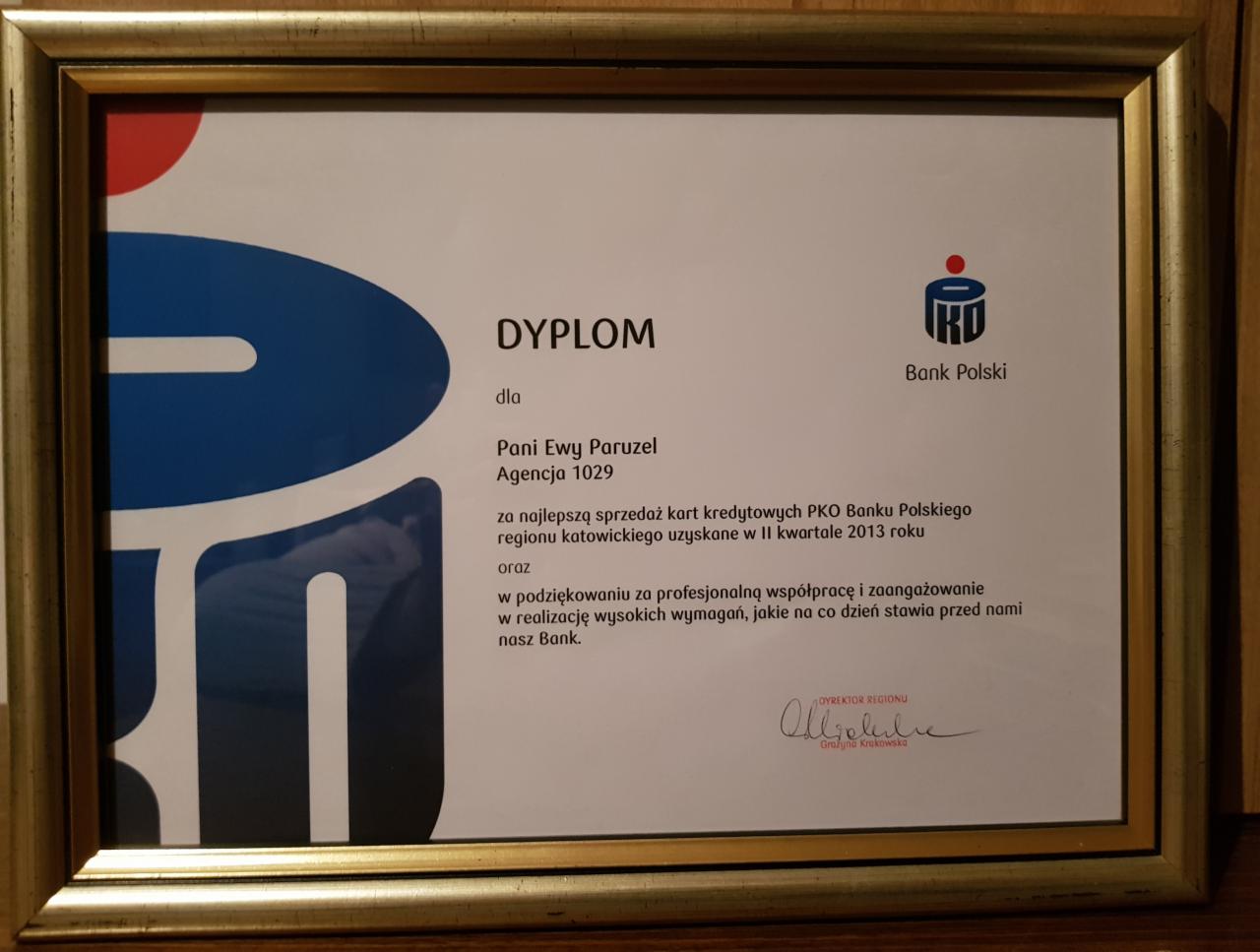 Oprawiony w złotą ramę dyplom uznania dla Pani Ewy Paruzel za najlepszą sprzedaż kart kredytowych PKO Banku Polskiego w regionie katowickim w II kwartale 2013 roku, z logo banku i podpisem...