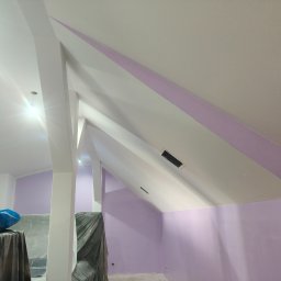 Marmał-Tech - Pomalowane na liliowo poddasze ze skośnym sufitem i widocznymi elementami konstrukcyjnymi. Część mebli zabezpieczona folią malarską. Widoczny fragment instalacji.