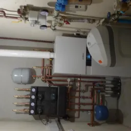 Zmontowana kotłownia w piwnicy w Markach, widoczne liczne rury miedziane, zbiornik buforowy, rozdzielacz i nowoczesny piec grzewczy.