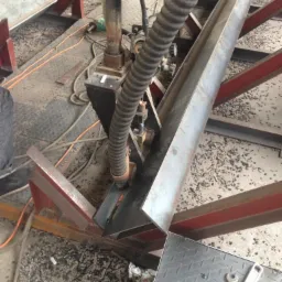 Proces spawania elementu konstrukcji stalowej, widoczny automat spawalniczy z podajnikiem drutu, fragment konstrukcji i klucz nastawny obok.