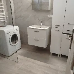 Jasna łazienka z marmurowymi płytkami, wiszącą szafką z umywalką, wysoką szafką i pralką Polar.